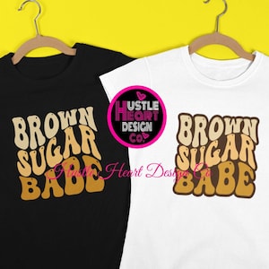 May include: Two t-shirts with the text "Brown Sugar Babe" in a retro font. The shirts are black and white and are hanging on hangers against a yellow background.