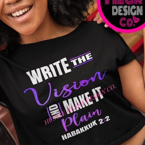 May include: A black crop top with the text "WRITE THE VISION AND MAKE IT PLAIN HABAKKUK 2:2" in white and purple lettering. The text is centered on the shirt. The shirt is being worn by a person with dark hair.