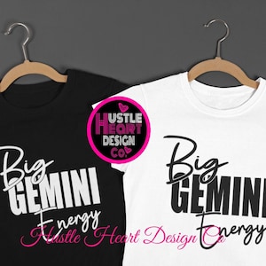 May include: Two t-shirts, one black and one white, hang on wooden hangers. Each shirt features the text "Big Gemini Energy" in a mix of script and block letters. The shirts are from Hustle Heart Design Co.