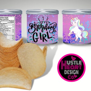 May include: A set of three pink and purple cans with a unicorn design and the text "Birthday Girl". The cans are decorated with glitter and iridescent paint splatters. The cans are sitting on a white surface.