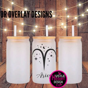 May include: Three frosted glass tumblers with bamboo lids and straws. The center tumbler has a black and white design of the zodiac sign Aries with stars and a crescent moon. The text "Aries" is written below the design. The text "Hustle Heart Design Co." is written below the design on the right tumbler.