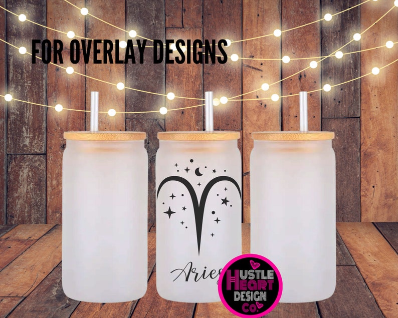 May include: Three frosted glass tumblers with bamboo lids and straws. The center tumbler has a black and white design of the zodiac sign Aries with stars and a crescent moon. The text "Aries" is written below the design. The text "Hustle Heart Design Co." is written below the design on the right tumbler.