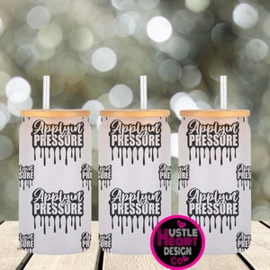 May include: Three white tumblers with bamboo lids and clear straws. Each tumbler has a black and white graphic that says "Applyin Pressure" with dripping paint. The tumblers are on a wooden surface.