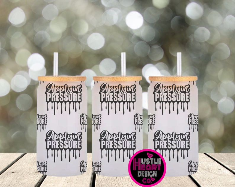 May include: Three white tumblers with bamboo lids and clear straws. Each tumbler has a black and white graphic that says "Applyin Pressure" with dripping paint. The tumblers are on a wooden surface.