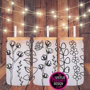 May include: Three frosted glass tumblers with bamboo lids and black floral designs. The tumblers are on a wooden surface with string lights in the background. The text "Hustle Heart Design Co." is visible in the lower right corner of the image.