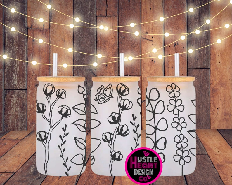 May include: Three frosted glass tumblers with bamboo lids and black floral designs. The tumblers are on a wooden surface with string lights in the background. The text "Hustle Heart Design Co." is visible in the lower right corner of the image.