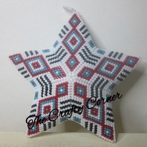 May include: A white star-shaped ornament with a geometric pattern in red, blue, and black. The ornament is made of beads and has a textured surface. The text "The Crafty Corner" is visible on the ornament.