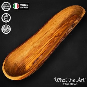 May include: A long, hand-carved olive wood bowl with a natural wood grain pattern. The bowl is labelled as Italian olive wood and features the text "What the Art!" and "Unique".