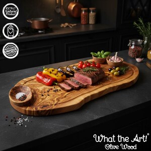 K&ouml;nnte beinhalten: Ein Servierbrett aus Olivenholz mit nat&uuml;rlicher Kante, das geschnittenes Steak, gegrilltes Gem&uuml;se, Oliven und Tomaten enth&auml;lt. Eine kleine Schale mit Salz und Pfeffer befindet sich an der Seite. Der Text "What the Art! Olive Wood" ist sichtbar.