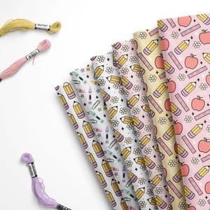 May include: A collection of fabric sheets featuring repeating patterns of yellow pencils, pink apples, rulers, and white flowers, accompanied by three separate skeins of embroidery floss in pale yellow, light pink, and light purple colors.