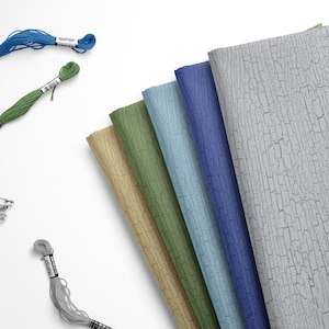 May include: Six fabric swatches with a cracked paint design in various colors, including gray, blue, green, and beige. The swatches are arranged in a fan shape. There are also spools of thread in blue, green, and gray, and a set of safety pins.