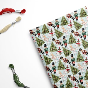 May include: A light blue background with a repeating pattern of nutcracker soldiers, ballerinas, candy canes, and Christmas trees. The pattern is in shades of red, green, white, and brown.