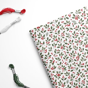 May include: A folded piece of white fabric featuring a repeating pattern of green leaves and red berries, accompanied by three individual skeins of embroidery floss in solid red, white, and dark green colors positioned nearby.