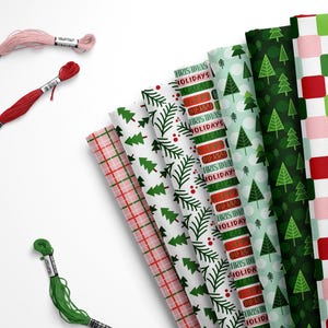 May include: A collection of Christmas-themed wrapping paper rolls with various patterns, including Christmas trees, plaid, and the text "HO HO HO". Three spools of embroidery floss in pink, red, and green are also visible.