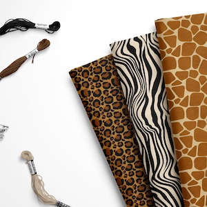 May include: Four fabric swatches with different animal print patterns: leopard, zebra, and giraffe. The swatches are arranged in a stack, with the giraffe print on top. There are also three spools of embroidery floss in black, brown, and beige.