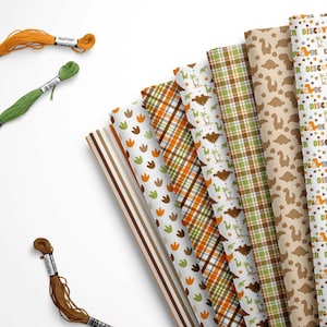 May include: An assortment of patterned fabric rolls with dinosaur and plaid designs in shades of brown, green, and orange. Three skeins of embroidery floss in orange, green, and brown are also visible.
