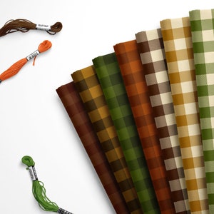 May include: Assortment of eight fabric swatches in various shades of brown, green, and orange with a plaid pattern. The fabric swatches are arranged in a fan shape. Three spools of embroidery floss in orange, green, and brown are also included.