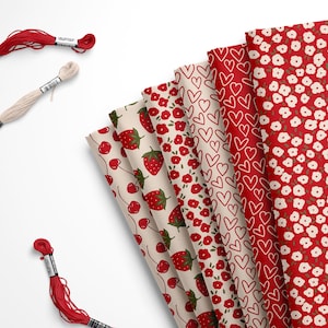 May include: An assortment of fabric patterns featuring strawberries, cherries, hearts, and floral designs in red and white. Three spools of embroidery floss in red and cream are also visible.
