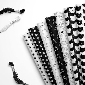 May include: A set of eight black and white fabric scraps featuring different cat-themed patterns. The patterns include paw prints, cats with different facial expressions, and cats with different body positions. The fabric scraps are arranged in a fan shape and are accompanied by two spools of black and white embroidery floss.