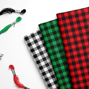 May include: Three different plaid fabrics in red and black, green and black, and white and black.  The fabrics are arranged in a stack with the red and black fabric on top.  There are also spools of red, green, and black thread and safety pins.