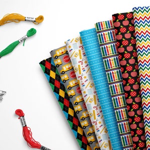 May include: A collection of eight different fabric prints featuring school-themed patterns, including school buses, crayons, apples, and schoolhouses. The fabrics are arranged in a fan shape and are accompanied by spools of embroidery floss in yellow, green, and red.