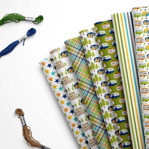 May include: An assortment of patterned paper rolls with camping and star designs, alongside spools of green, blue, and brown embroidery floss. The paper rolls feature text that reads "Home Sweet Camper".