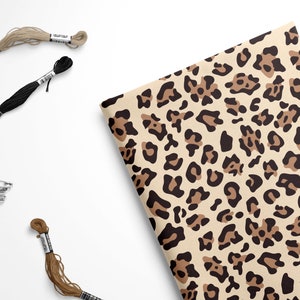 May include: A sheet of brown and black leopard print wrapping paper. The paper is lying on a white surface with spools of embroidery floss in brown and black.