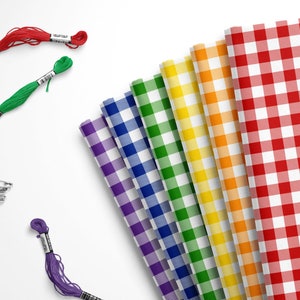 May include: A rainbow assortment of gingham fabric swatches in purple, blue, green, yellow, orange, and red.  The fabric is folded and arranged in a fan shape.  There are also spools of embroidery floss in red, green, and purple.