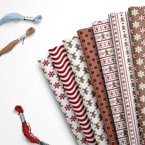 May include: A collection of eight different patterned wrapping paper featuring gingerbread men, snowflakes, candy canes, and red and white stripes. The paper is arranged in a fan shape with the edges of the paper overlapping. Three spools of embroidery floss are also included in the image.