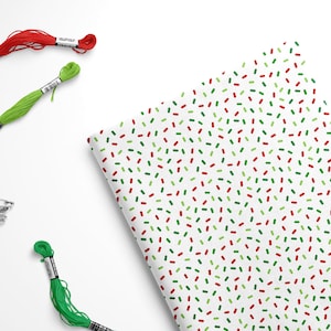 May include: A sheet of white wrapping paper with a repeating pattern of red and green confetti. There are three spools of embroidery floss, one red, one green, and one green with a white label.