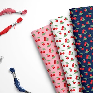 May include: Three fabric swatches with a repeating pattern of red cherries on green leaves. The swatches are on a white background. The fabric swatches are pink, white, and navy blue.