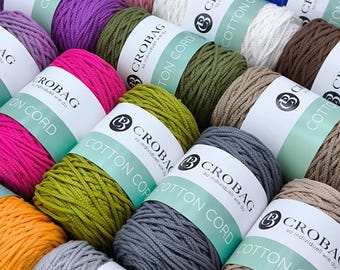 May include: A collection of colorful cotton cord spools in various shades, including pink, green, purple, and gray. Each spool is labeled with the brand name "CROBAG" and "COTTON CORD". The image showcases a variety of crafting supplies.
