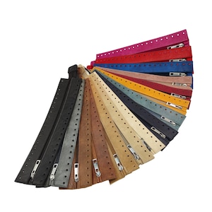 Könnte beinhalten: Eine Auswahl an Reißverschluss-Zippern in verschiedenen Farben, darunter Schwarz, Grau, Braun, Beige, Blau, Rot und Pink. Die Reißverschluss-Zipper sind aus Leder gefertigt und haben ein perforiertes Design.