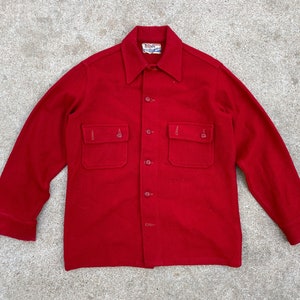 May include: A red wool shirt with a button-up front and two large pockets. The shirt has a label that reads "Elsie's" and "Made in USA".