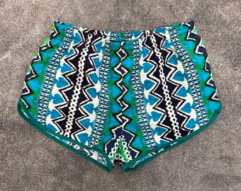 May include: Blue, green, white, and black patterned athletic shorts with a green trim. The shorts have an elastic waistband.