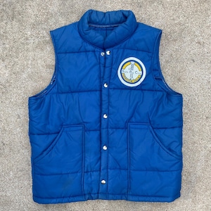 Może przedstawiać: Niebieska pikowana kamizelka zapinana na zatrzaski z naszywką z przodu z napisem "Santa Rio Corp. Fairview Grill".