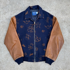 May include: A blue and brown varsity jacket with leather sleeves. The jacket has a zip fastening and a pattern of Native American-inspired designs on the front.