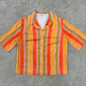 May include: A short-sleeved button-down shirt with a striped pattern in shades of orange, yellow, and brown. The shirt has a collar and a button-up front.