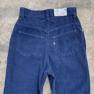 May include: A pair of dark blue corduroy pants with a small white label on the back waistband. The label says "Sanforized", "Made in U.S.A.", and "Levi's Trademark".