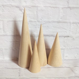 May include: Four wooden cone-shaped ring holders in various sizes, arranged on a white brick background.