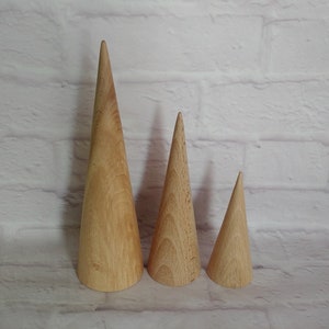 May include: Three wooden cone-shaped decorative objects of varying sizes. The cones are made of light-colored wood and have a smooth, polished finish. They are arranged in a row, with the largest cone on the left and the smallest on the right.