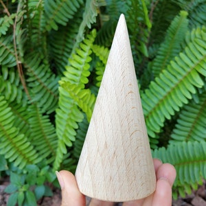 May include: A light wood cone-shaped ring holder. The holder is made of natural wood and has a smooth, polished finish.
