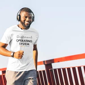 Może przedstawiać: Biały t-shirt z nadrukiem "Different Operating System" na przodzie. Tekst jest czarny z tęczowym wzorem pod spodem.