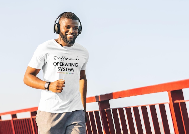 Może przedstawiać: Biały t-shirt z nadrukiem "Different Operating System" na przodzie. Tekst jest czarny z tęczowym wzorem pod spodem.