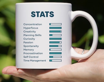 May include: White ceramic mug with a black and teal graphic that reads "STATS" and lists various skills with a bar graph rating system. The skills listed are Concentration, Hyperfocus, Creativity, Planning Skills, Curiosity, Passion, Spontaneity, Memory, Procrastination, Self Control, and Time Management.
