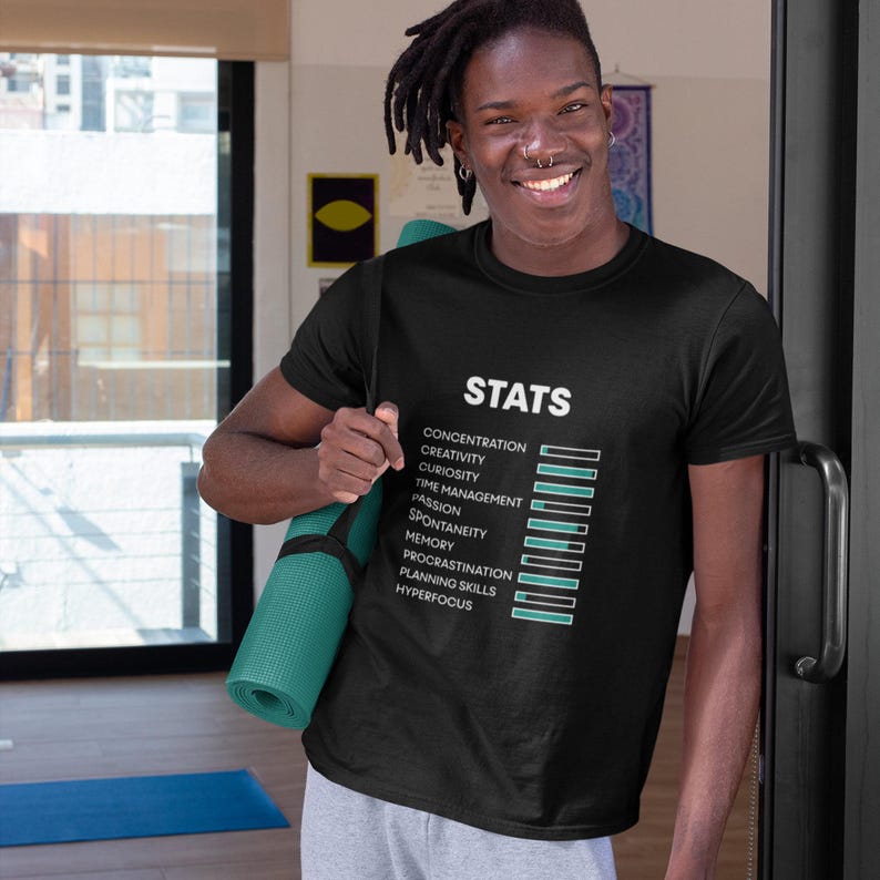 May include: A black short-sleeved t-shirt featuring the white text "STATS" above a list of attributes including concentration, creativity, curiosity, time management, passion, spontaneity, memory, procrastination, planning skills, and hyperfocus.