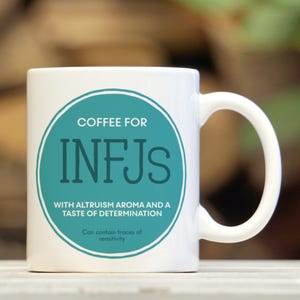May include: White ceramic coffee mug with a teal circle containing the text "COFFEE FOR INFJS" and the words "WITH ALTRUISM AROMA AND A TASTE OF DETERMINATION". The text "Can contain traces of sensitivity" is printed below the circle.