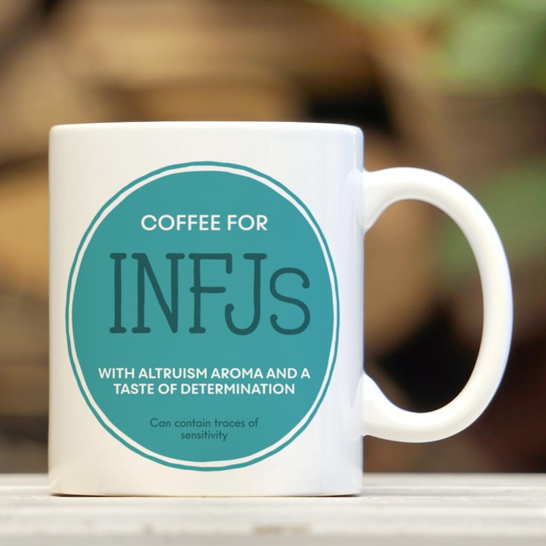 May include: White ceramic coffee mug with a teal circle containing the text "COFFEE FOR INFJS" and the words "WITH ALTRUISM AROMA AND A TASTE OF DETERMINATION". The text "Can contain traces of sensitivity" is printed below the circle.
