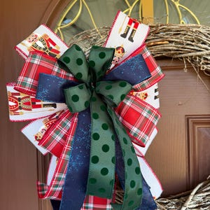May include: A Christmas wreath with a large bow made of red and green plaid ribbon, green velvet ribbon with white polka dots, blue ribbon with white snowflakes, and white ribbon with a nutcracker pattern.