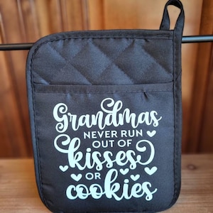 May include: Black quilted oven mitt with the text "Grandmas never run out of kisses or cookies" in white script. The mitt has a pocket and a hanging loop, perfect for kitchen use.